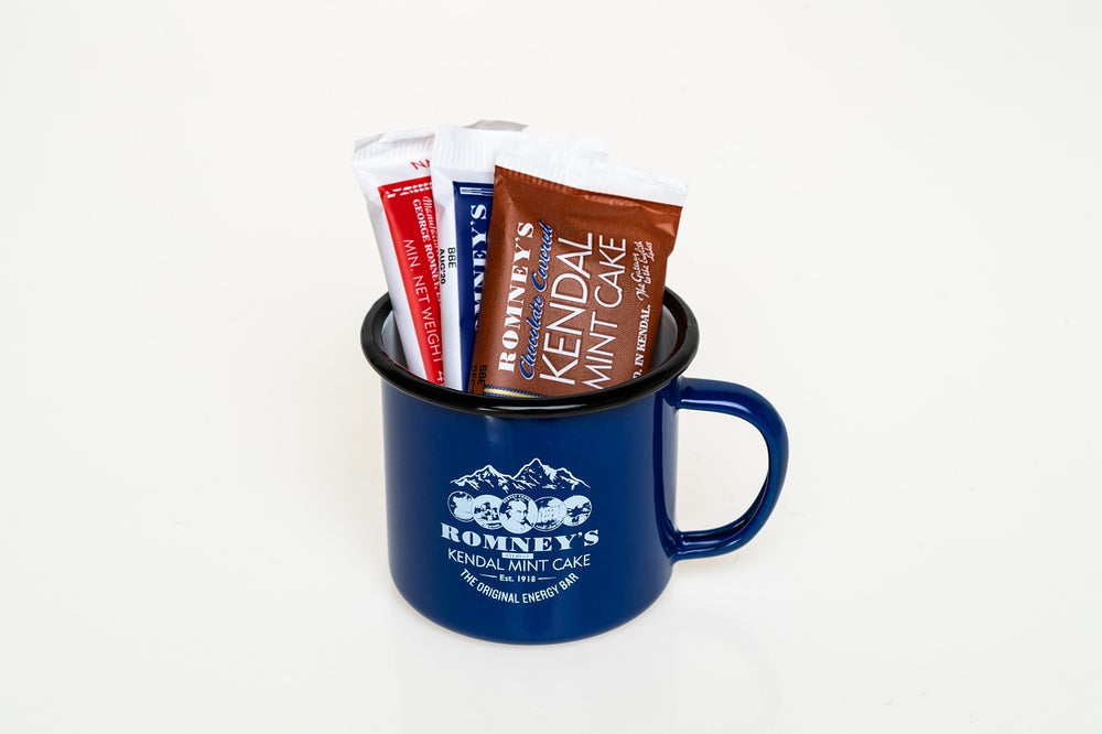 A product image showing a blue mug standing up and featuring the Romney's logo on its side. Three small bars of wrapped Romney's Kendal Mint Cake are inside the mug. The bars are Chocolate, White & Brown flavoured Kendal Mint Cake.