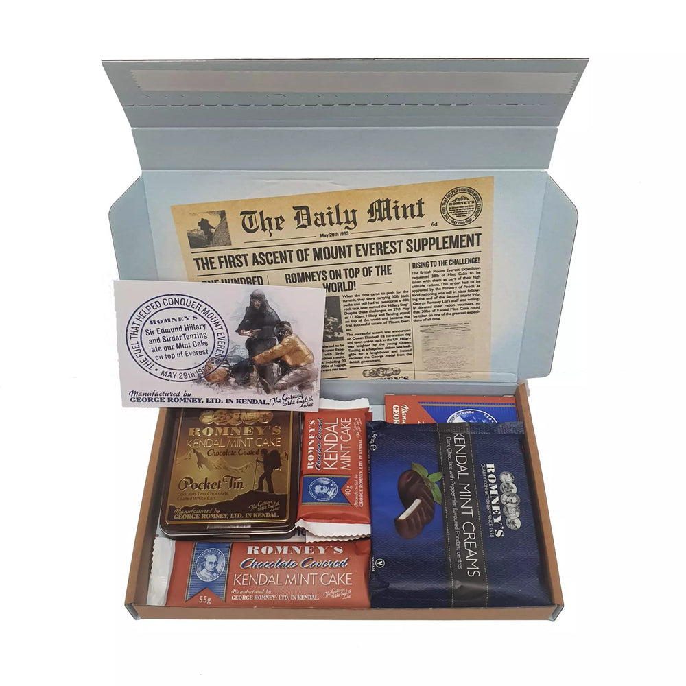 An open rectangular cardboard box containing a variety of Romney's confectionery products such as: 55g chocolate coated kendal mint cake, two 40g chocolate kendal mint cake bars, 220g chocolate coated kendal mint cake bar, a chocolate coated pocket tin, kendal mint creams