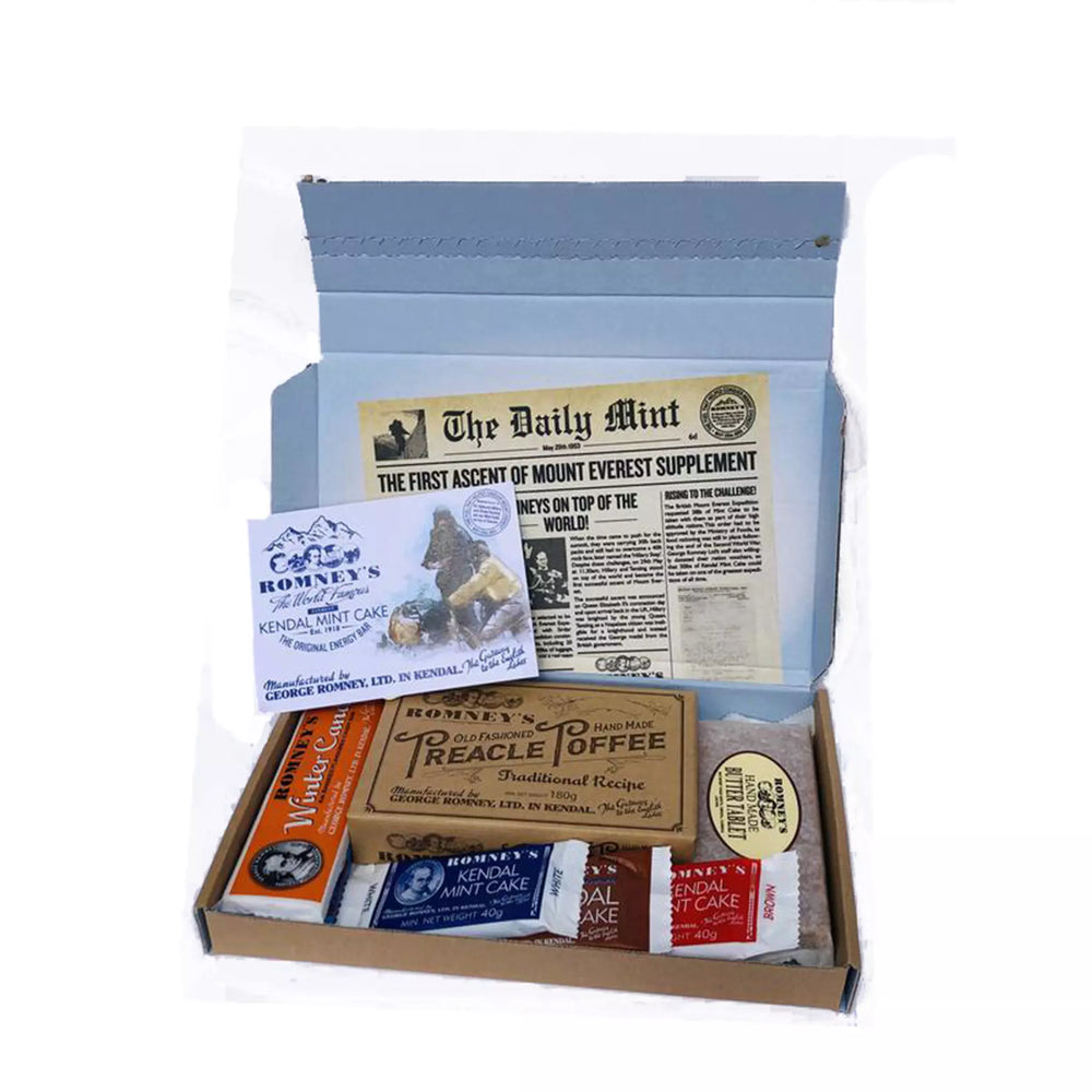 An open rectangular cardboard box containing a variety of Romney's confectionery products such as: rum and butter bar, winter candy bar, 40g white kendal mint cake, 40g brown kendal mint cake, 40g chocolate coated kendal mint cake, butter tablet bar, box of old fashioned treacle toffee