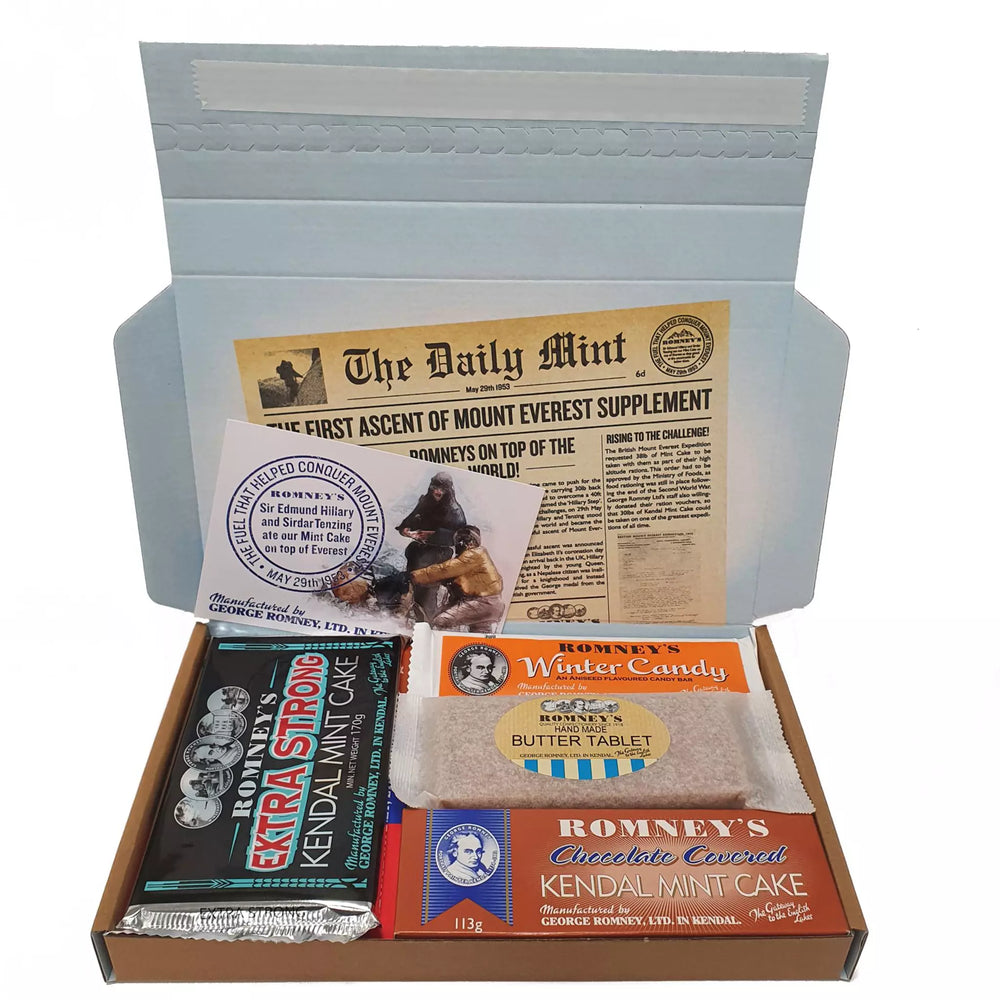 An open rectangular cardboard box containing a variety of Romney's confectionery products such as: Rum & Butter Bar, Winter Candy Bar, Butter Tablet Bar, Extra Strong Kendal Mint Cake Bar, 113g Chocolate Coated Kendal Mint Cake Bar, 227g Triple Kendal Mint Cake, Kendal Mint Creams